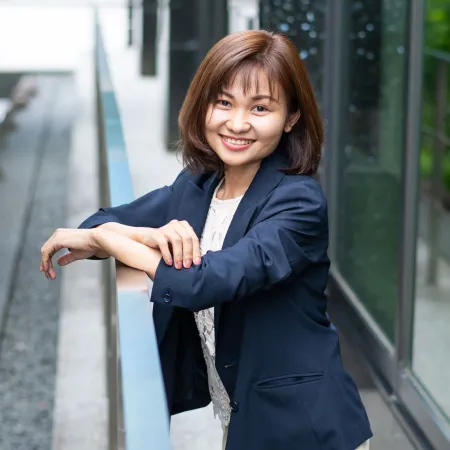 Photo of Seng Mai wearing a blue jacket smiling while leaning over a metal railing outside