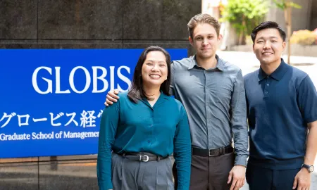Three diverse, smiling students posing together in front of a blue GLOBIS University sign