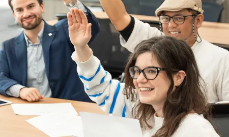 A diverse group of students smiling and raising their hands enthusiastically during an interactive classroom session.