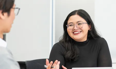 A woman with glasses smiling and engaging in a face-to-face discussion with a peer during a business workshop.