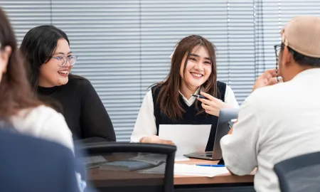 Two female students smile and engage in a collaborative class discussion with a male peer.