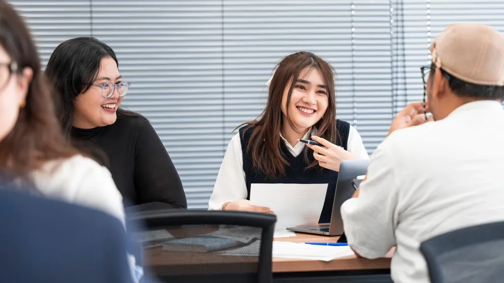 Two female students smile and engage in a collaborative class discussion with a male peer.